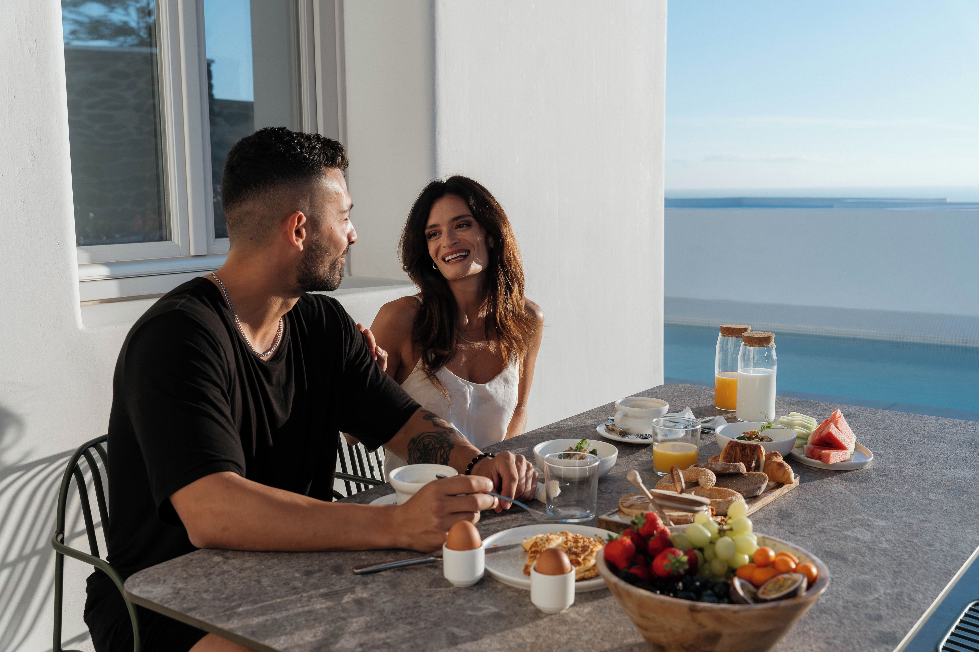 A dining table with breakfast items, a view of the sea, and a window with a view of the sea.