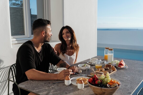 Une table à manger avec des aliments pour le petit-déjeuner, une vue sur la mer et une fenêtre donnant sur la mer.