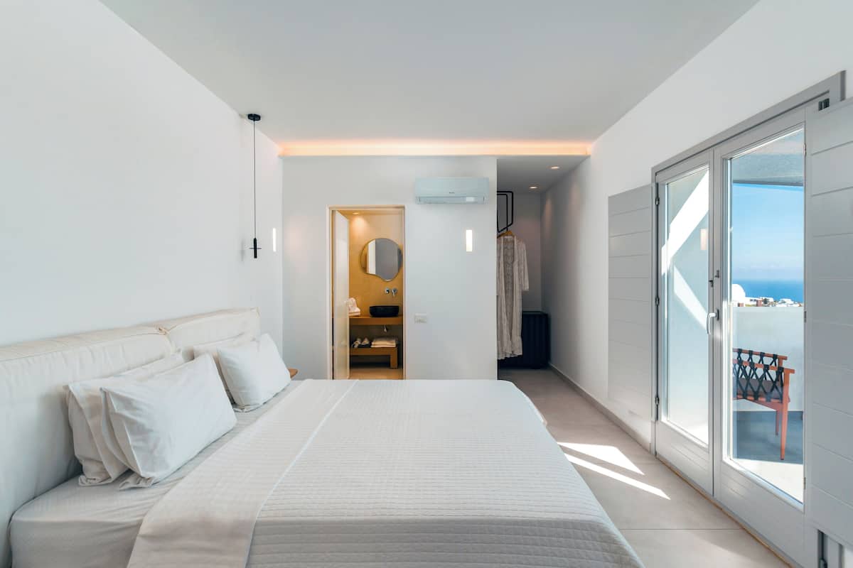 A modern bedroom with a large bed, a walk-in closet, and a balcony with a view.