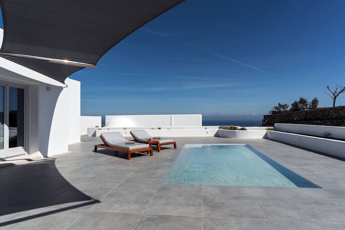 A rooftop pool area with two lounge chairs, a small pool, and a clear view of the ocean.