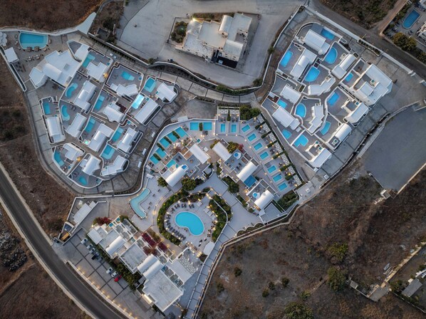 An aerial view of a resort with multiple swimming pools, guest rooms, and a central courtyard. - Oikos Santorini Living Concept (Santorini)