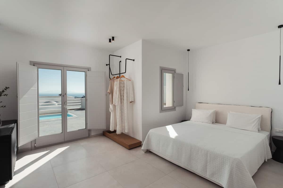 A modern bedroom with a large bed, a walk-in closet, and a view of the sea through a sliding door.