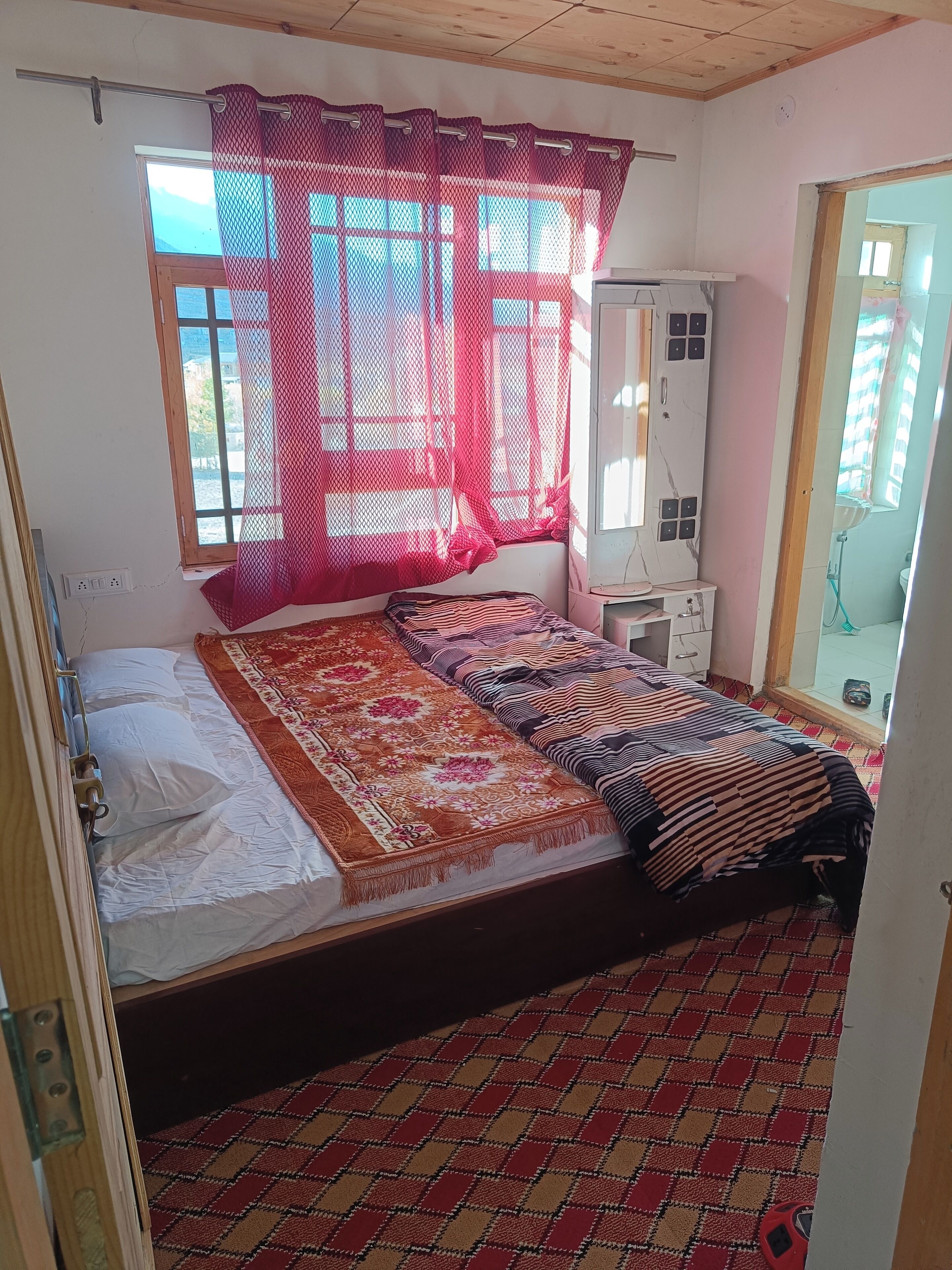 Una habitación con cama, un escritorio pequeño, un espejo y una ventana con cortina.