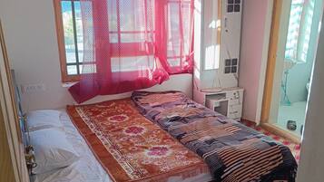 Una habitación con cama, un escritorio pequeño, un espejo y una ventana con cortina.