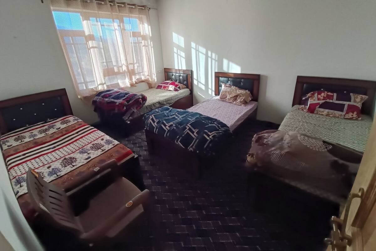 A room with three beds, a small desk, and a window with curtains.