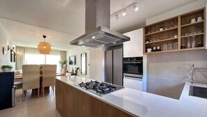 A modern kitchen with a central island, built-in oven, and a dining area with chairs and a table.
