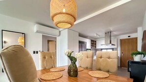 A dining area with a wooden table, beige chairs, woven placemats, and a vase with white flowers.