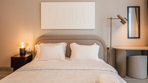 Une chambre à coucher moderne avec un lit, une table de chevet, une lampe et une œuvre d’art encadrée accrochée au mur.