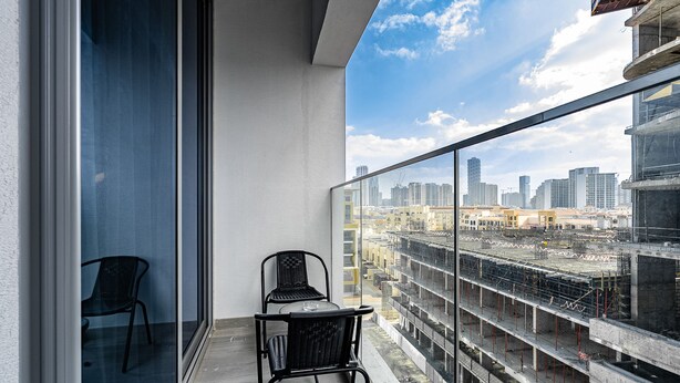 Een balkon met glazen hekwerk, twee stoelen en een tafel.