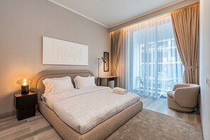 A modern hotel room with a large bed, a nightstand with a lamp, a chair, and a view of the city through sheer curtains. - Concept 7 211 in Dubai (Dubai)