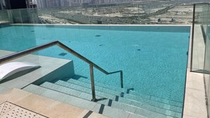 A rooftop pool with clear blue water, a glass railing, and a view of a city skyline. - Berkley Place 905 in Dubai (Dubai)