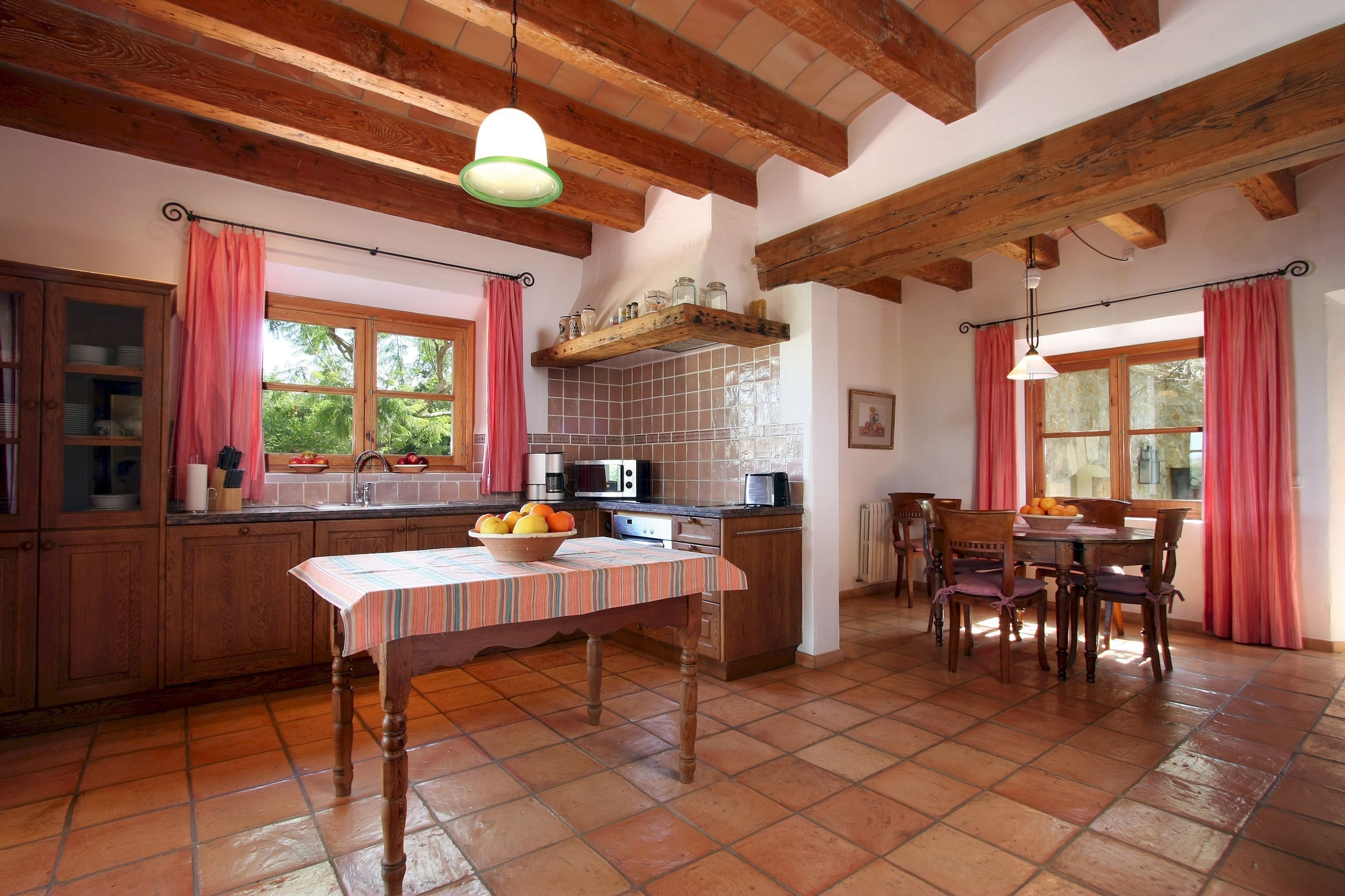 A kitchen with wooden cabinets, a tiled backsplash, a dining table with chairs, and a hanging light fixture.