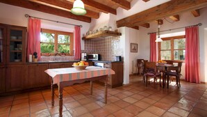 A kitchen with wooden cabinets, a tiled backsplash, a dining table with chairs, and a hanging light fixture. - Villa Reco de Marina (Sa Pobla)