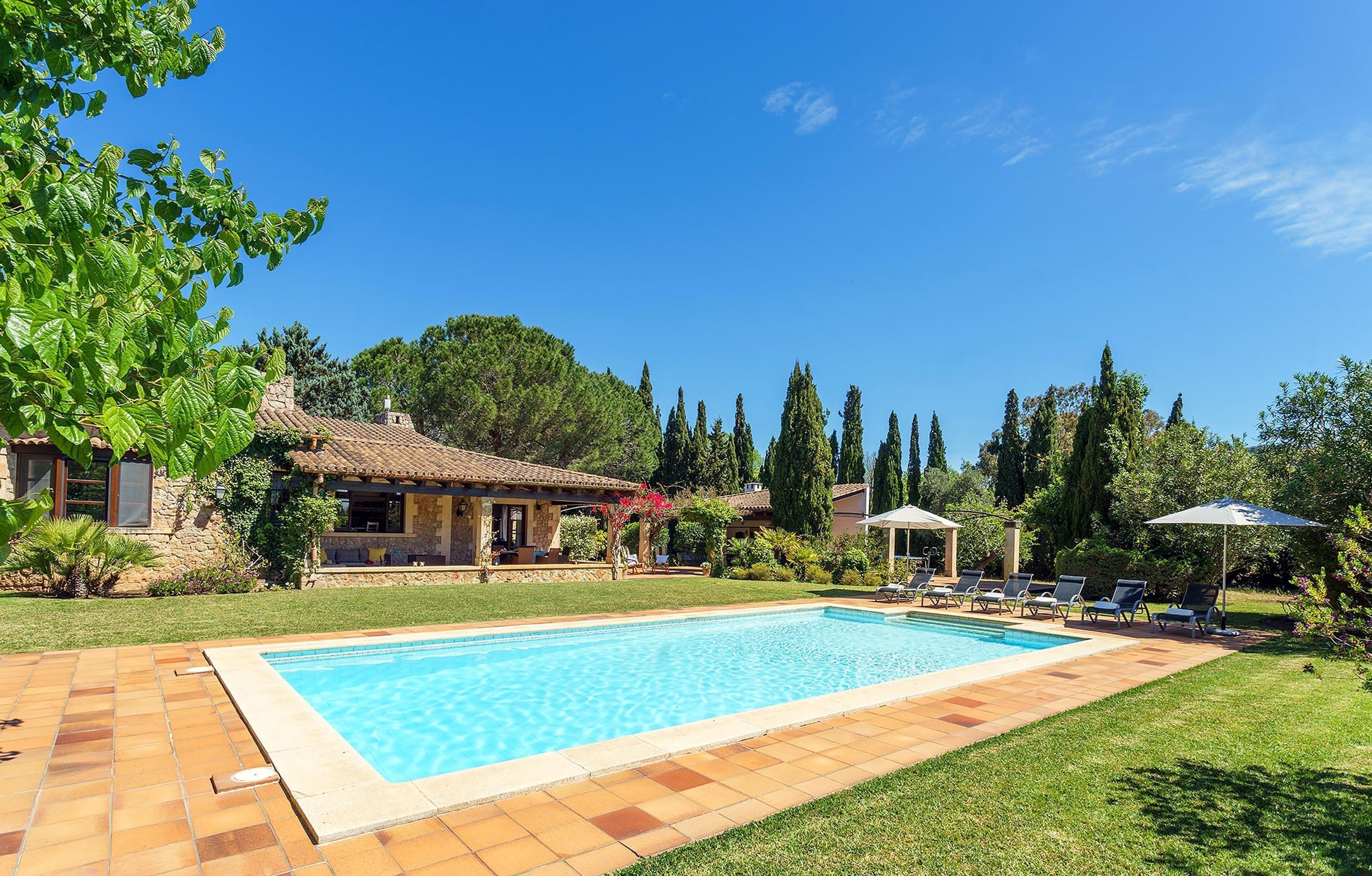 A swimming pool with a tiled deck, surrounded by a well-maintained lawn and trees.