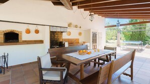 Un espace extérieur aménagé pour les repas, avec un four en briques, du mobilier en bois et une vue sur le jardin.