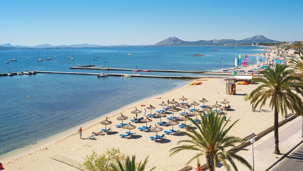 A beach with clear blue water, boats, and umbrellas. - Villa Playa in Port de Pollen a (Pollenca)