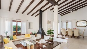 A spacious living room with a high ceiling, a fireplace, a dining area with a table and chairs, and a sofa with cushions. - Villa Playa in Port de Pollen a (Pollenca)