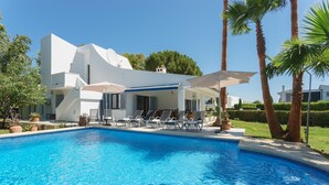 A modern pool area with a clear blue pool, lounge chairs, and a white building with a covered patio. - Villa Playa in Port de Pollen a (Pollenca)