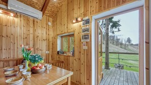 A wooden interior with a dining table set with bowls, a vase with flowers, and a fruit bowl. There is a window with a view of a grassy area and trees. - Wooden Chalet Kalanka in Nature (Kanal)