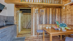 A wooden interior with a dining table set for four, a kitchen area with modern appliances, and a staircase leading to an upper level. - Wooden Chalet Kalanka in Nature (Kanal)