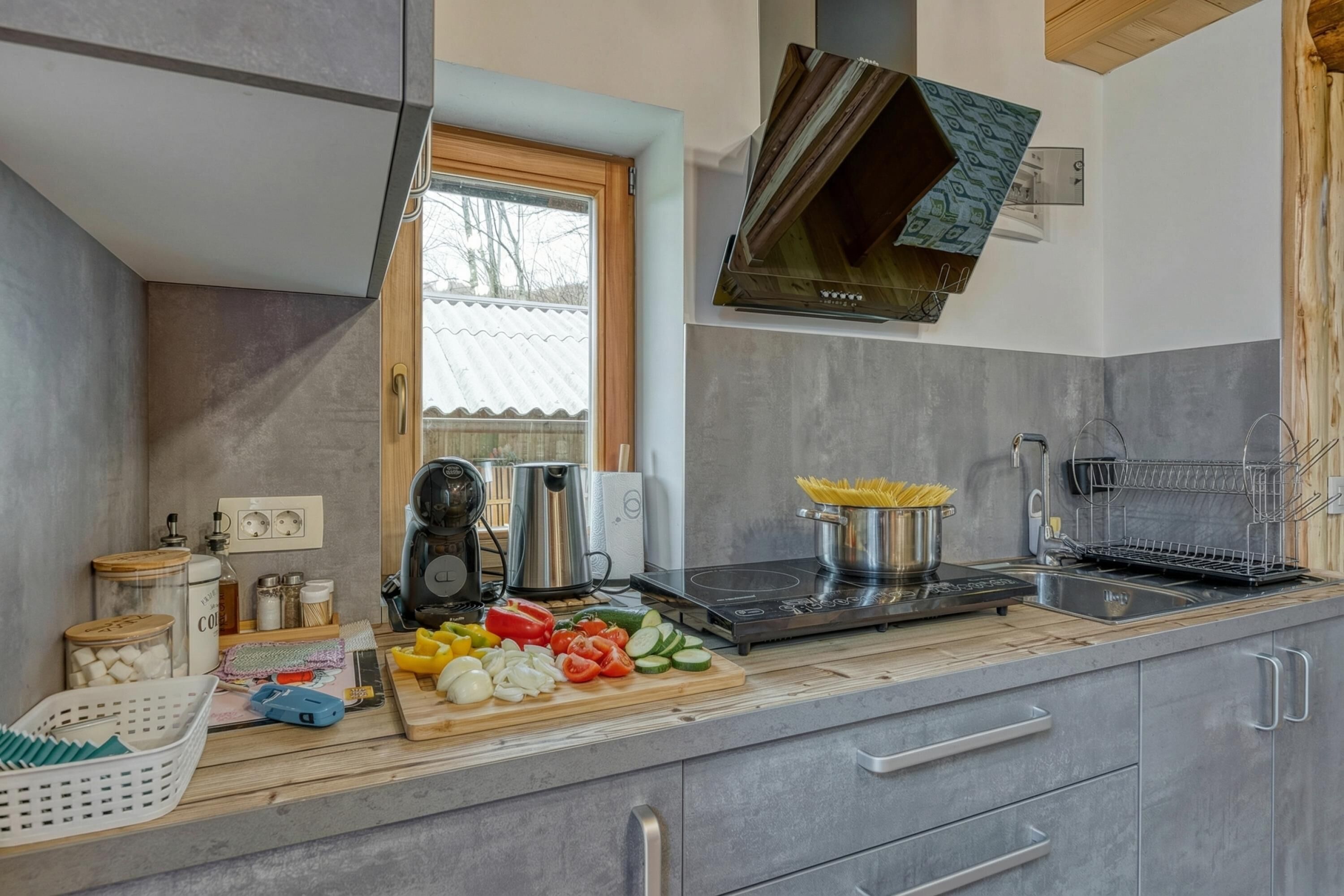 Une cuisine moderne équipée d’une cuisinière intégrée, d’une machine à café et d’une variété de légumes frais disposés sur le plan de travail.