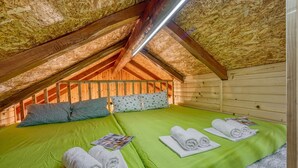An attic bedroom with two beds, green bedding, wooden walls, and a sloped ceiling. - Wooden Chalet Kalanka in Nature (Kanal)