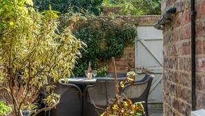 Un patio al aire libre con mobiliario de mimbre, una mesa con copas de vino y una pared de ladrillo con plantas.