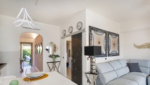 A modern living room with a grey sofa, a white coffee table, and a TV stand with a flat-screen TV. There are three clocks on the wall and a decorative wall hanging. - Elegant sea View Apartment by Wonderful Italy (Rapallo)