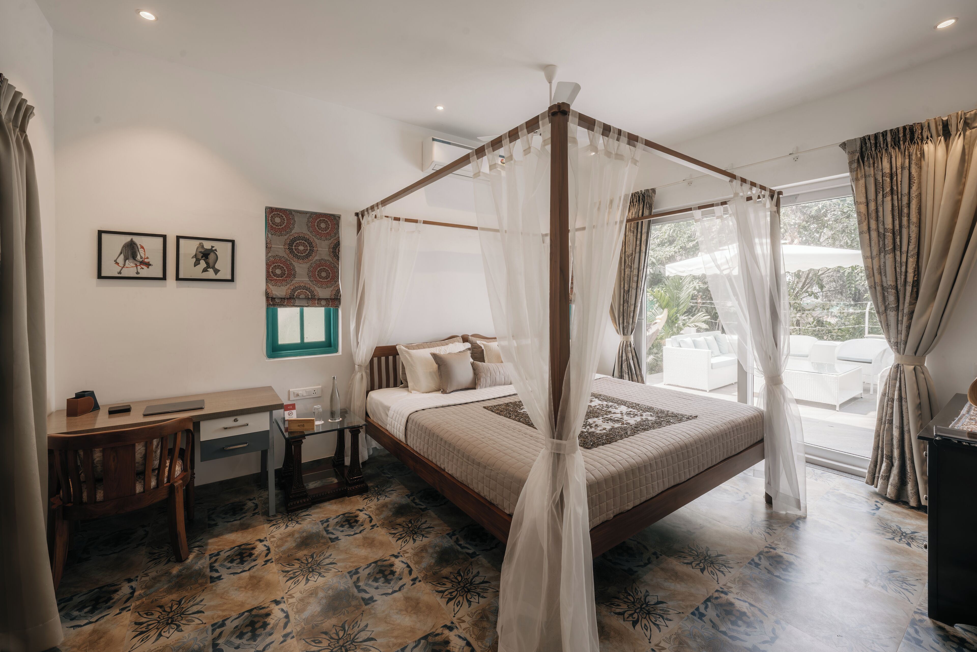 Una cama con dosel y cuatro columnas con vistas al exterior, un escritorio con silla y suelo estampado.