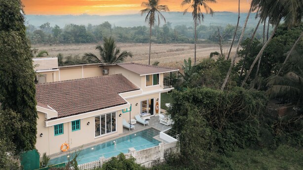 A house with a swimming pool, surrounded by palm trees and a view of the sunset. - Amã Stays & Trails Assa 360, Goa (Anjuna)