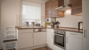 A modern kitchen with white cabinetry, a built-in oven, and a window with a view of the city. - Beautiful vacation home "Nele"! Perfect for the family (Geeste)