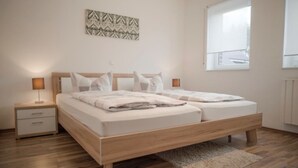 A double bed with a wooden frame and a headboard, two bedside tables, a floor lamp, and a window with blinds. - Beautiful vacation home "Nele"! Perfect for the family (Geeste)