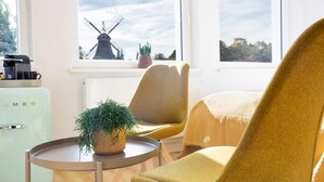 Una habitación con un refrigerador de estilo vintage, una mesa redonda con una planta en maceta y una silla con una manta.