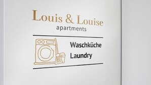 Logo de 'Louis & Louise apartments' con una lavadora e icono de lavandería, que indica servicios de lavandería.
