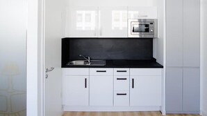 Una cocina compacta con armarios blancos, encimera negra y microondas integrado.