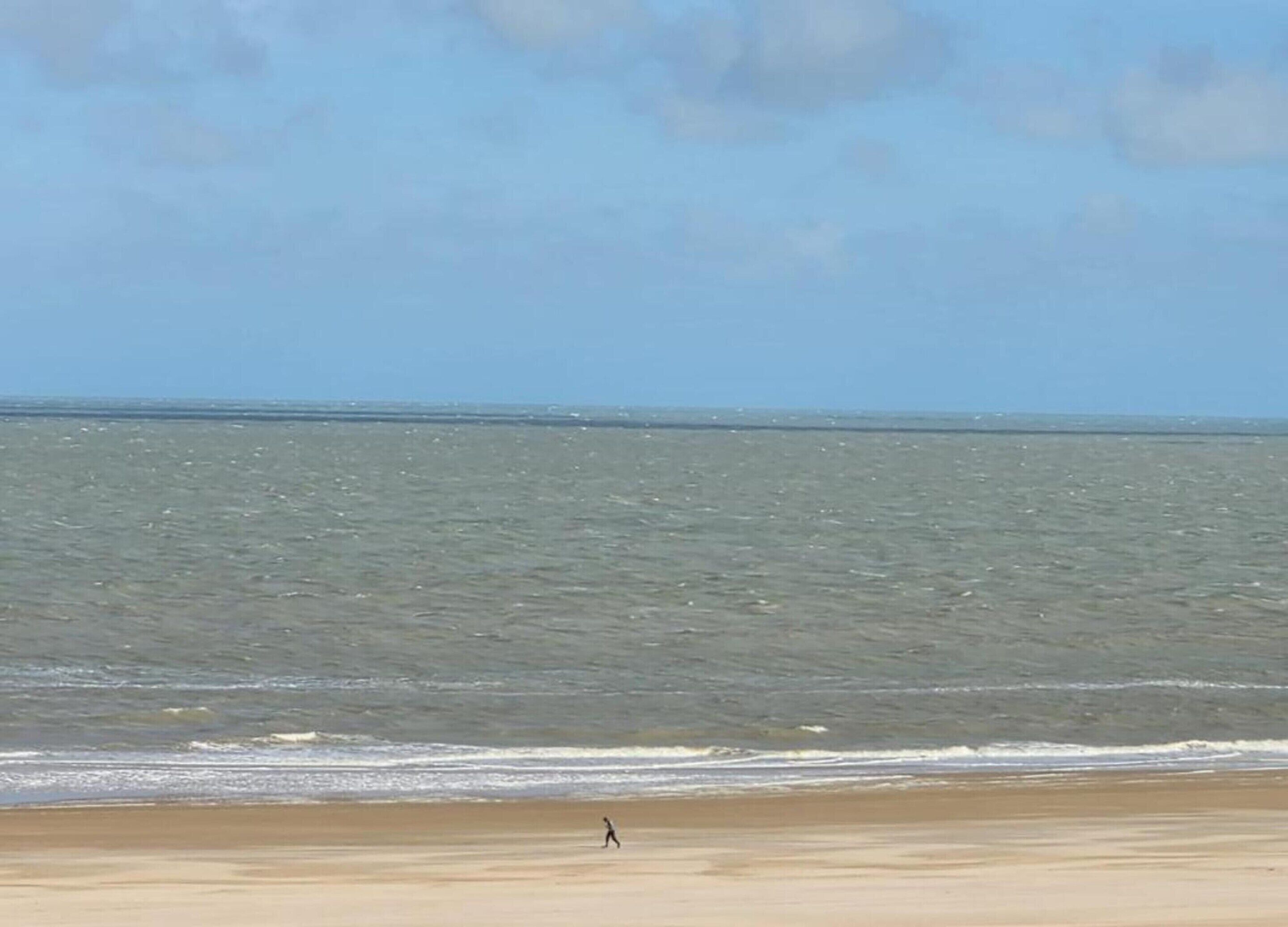 Een strand met een persoon die langs de kust wandelt.