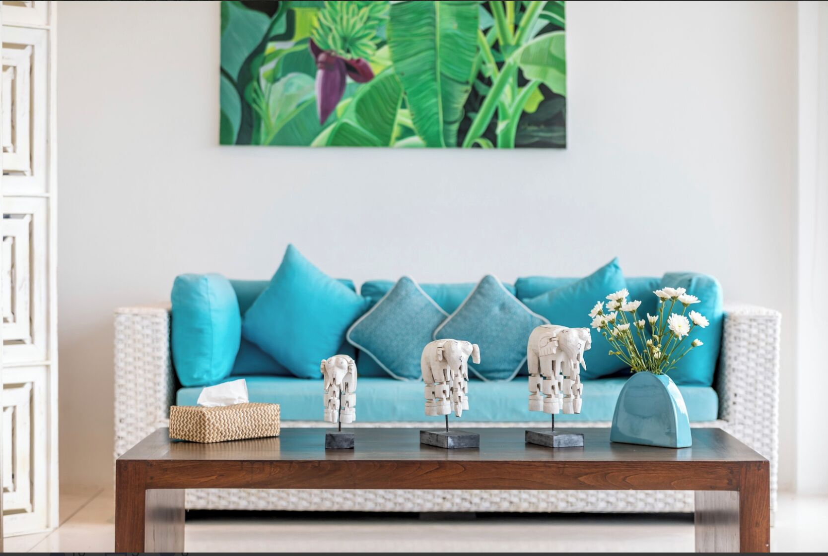 A living room with a blue sofa, teal cushions, a wooden coffee table, and decorative elephant sculptures.