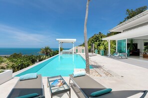 Un espace piscine moderne avec vue sur l’océan, des chaises longues et un coin salon abrité.
