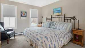 A bedroom with a bed, a chair, a nightstand, a lamp, and a painting on the wall.