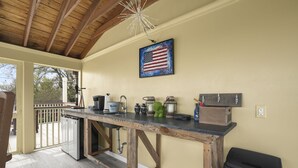 A kitchen with a wooden countertop, a sink, and a refrigerator. There is a hanging American flag and a wooden cabinet.