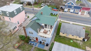 A two-story house with a green roof, a front porch, and a small deck.