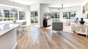 A spacious living room with a large window, a white sofa, a coffee table, and a TV.