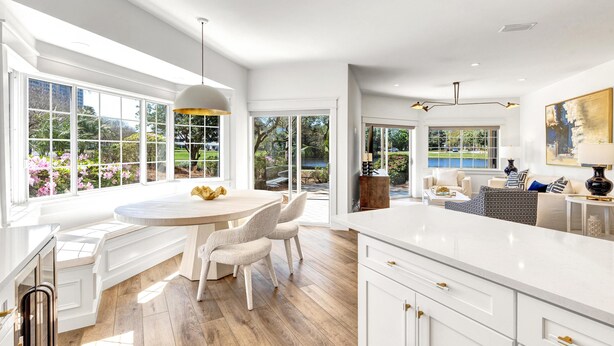 A spacious kitchen with a large island, white cabinetry, and a view of a garden and pool.