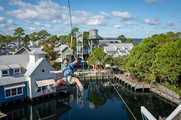A person zip-lining over a water body with buildings and trees in the background.