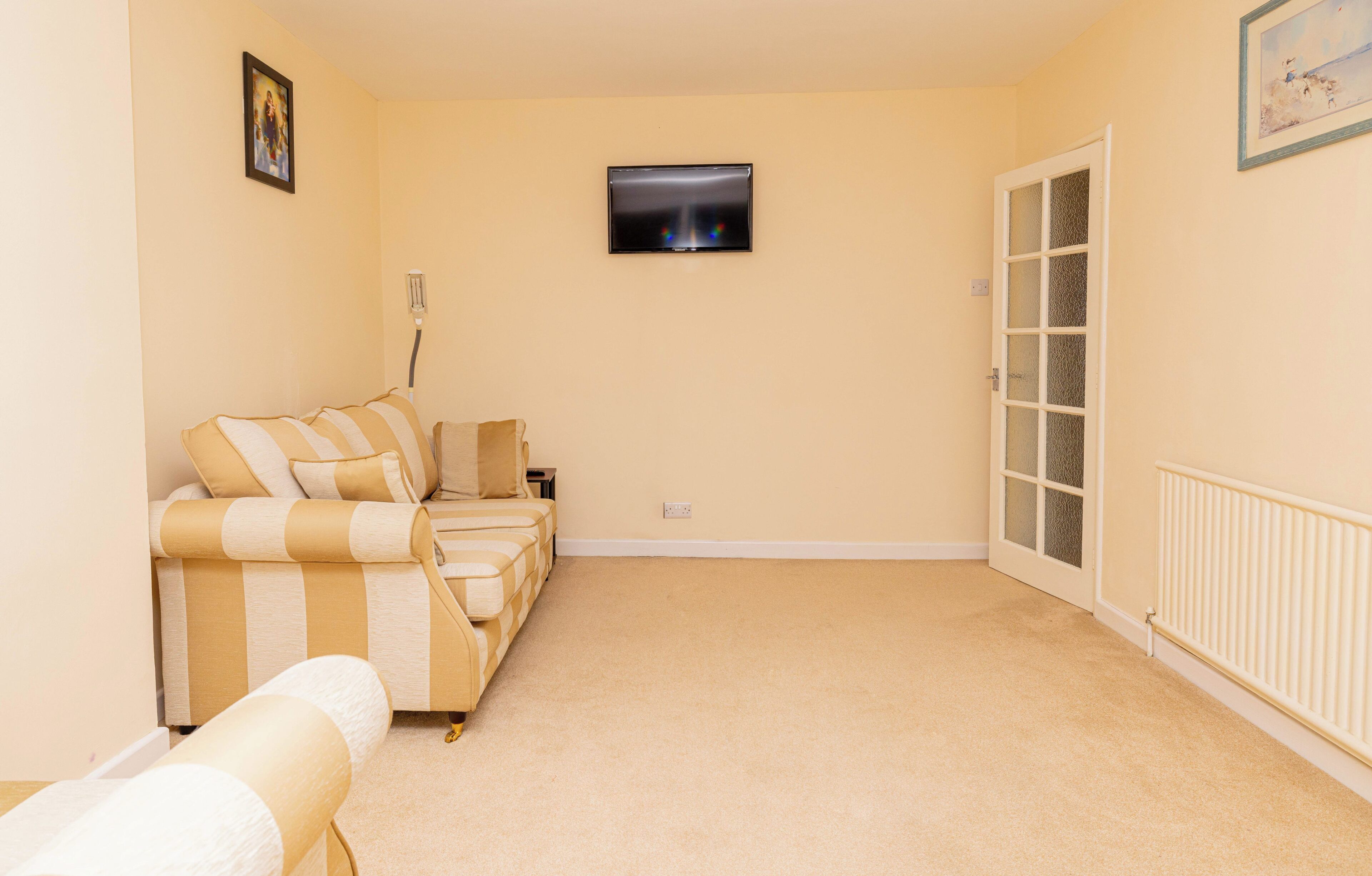 A living room with a beige sofa, a television mounted on the wall, and a door with frosted glass panels.
