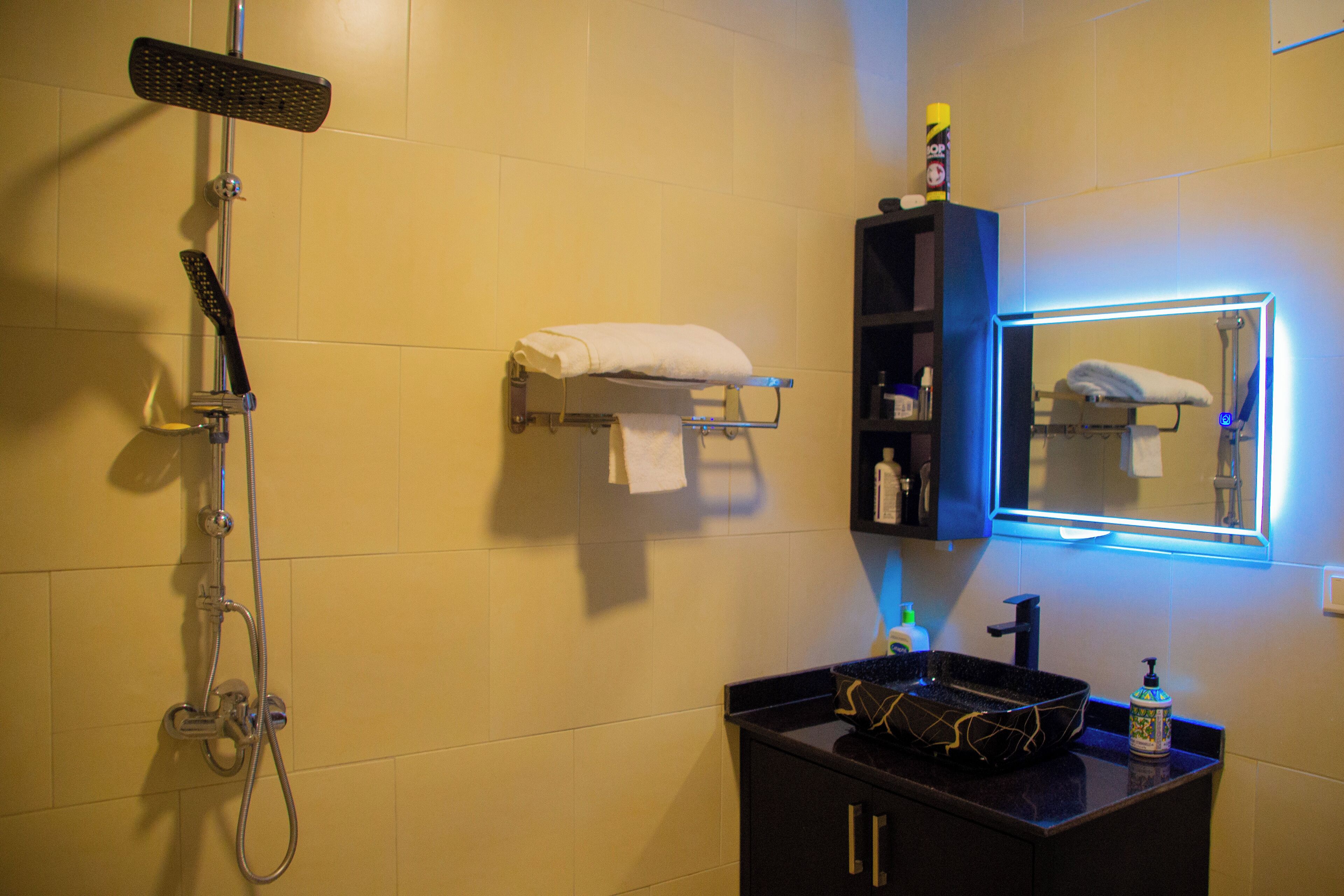 Un baño con ducha, un lavamanos con dispensador de jabón y un espejo con luz.