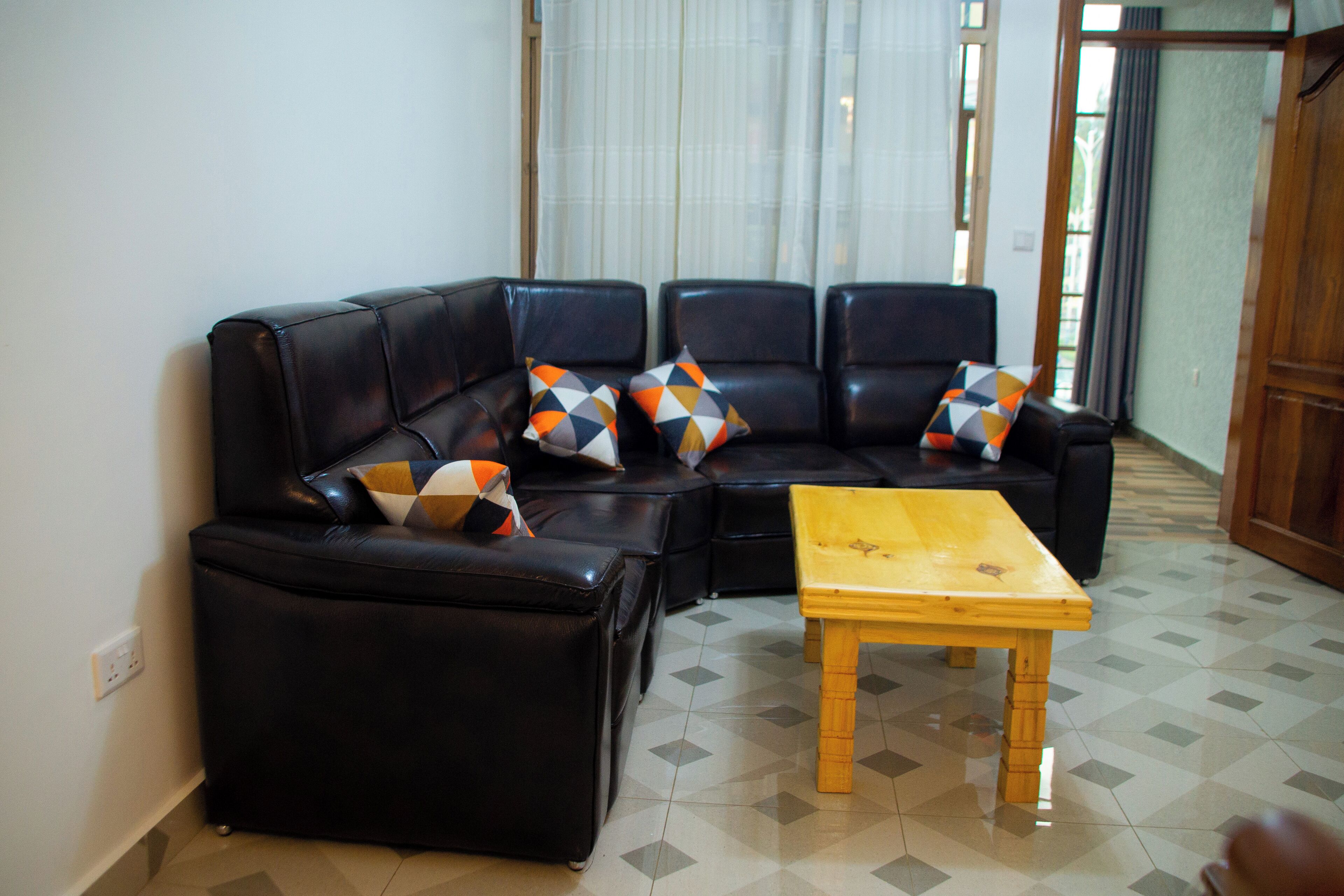 Un salon avec un canapé d’angle en cuir noir, une table basse en bois et des coussins décoratifs à motifs.