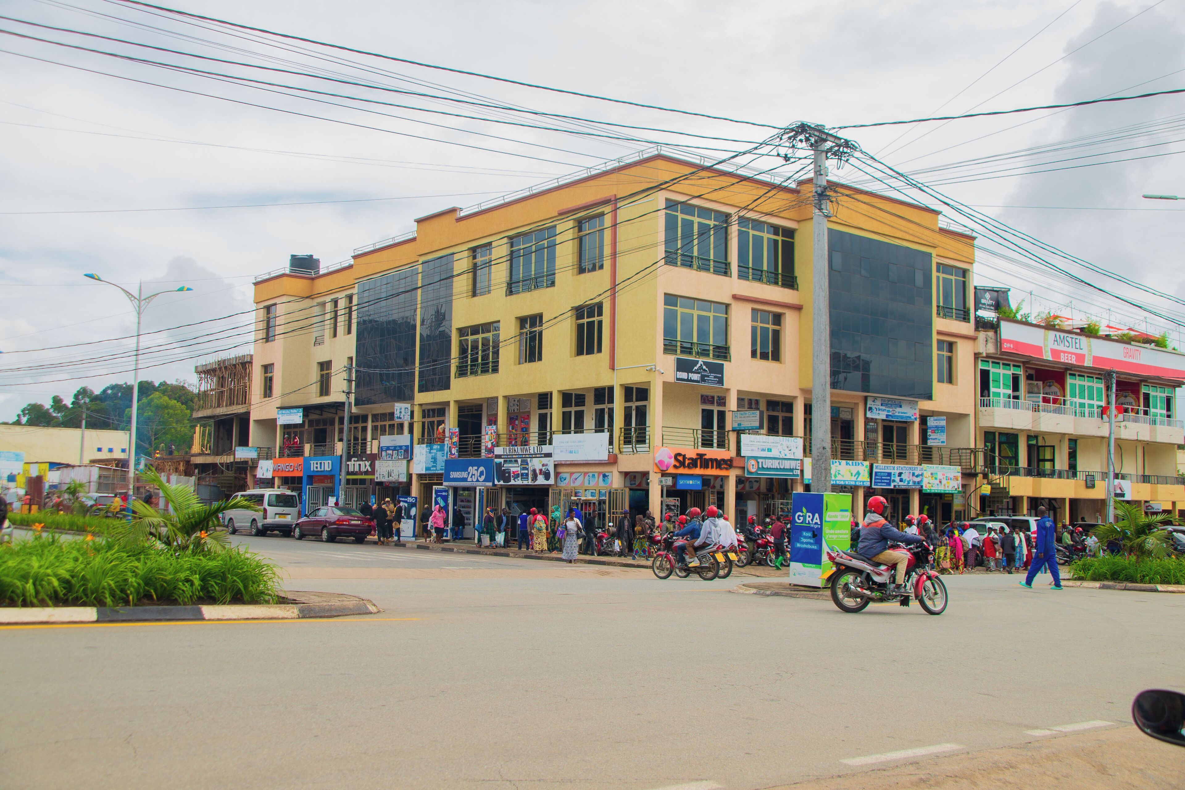 A multi-story building with various shops on the ground floor, including a visible pharmacy and a newsstand.
