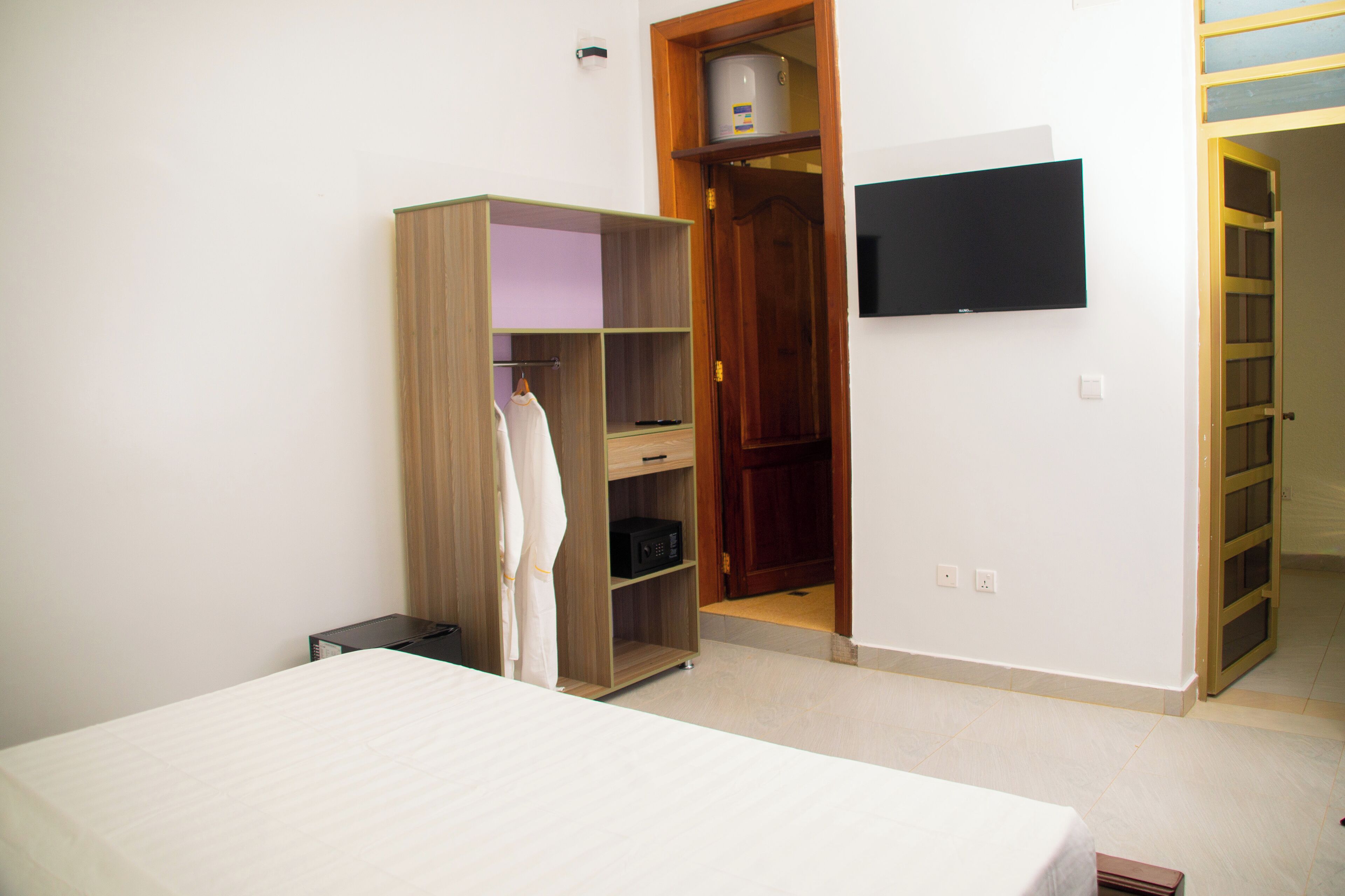 Une chambre à coucher comprenant un lit, une armoire, un téléviseur et une porte donnant sur une autre pièce.