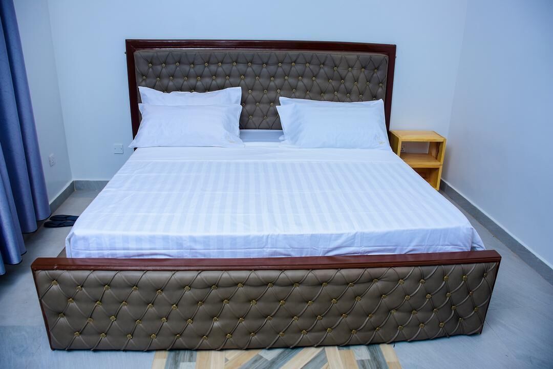 A neatly made bed with a tufted headboard and a wooden footboard, accompanied by a small wooden nightstand.